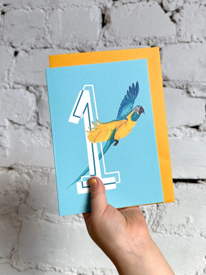 a bright blue card with a big white number 1 and an illustration of a macaw with a yellow envelope