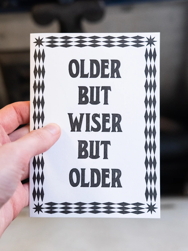 Letterpress card with text design, "Older but wiser but older," bordered by art-deco pattern of diamonds and stars.