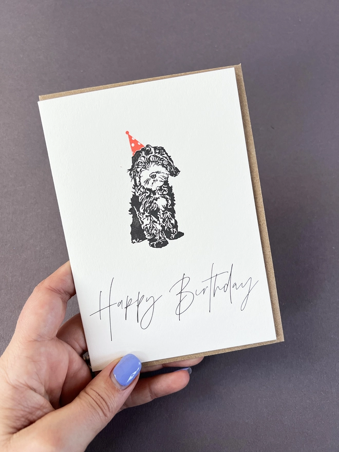 The very cute and fluffy Cockapoo puppy in a neon orange party hat with "Happy Birthday" beautifully written in a modern calligraphy underneath.