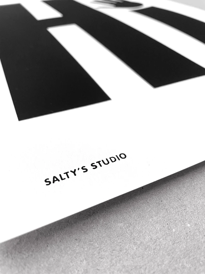 Close up of bottom left corner of a screen print sat on a grey background - showing the printed detail of the name Salty's Studio.