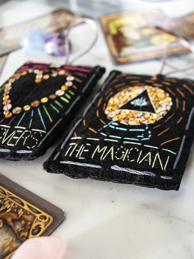 A handcrafted felt ornament with sequins and embroidery depicting "The Magician" tarot card. Colourful embroidery with an eye inside a crystal ball. Also accompanied by “The Empress and The Lovers”