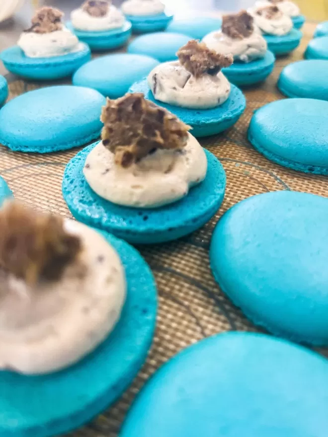 several blue macaron shells in a row showing the inside filling of a white cream filling and a cookie dough centre
