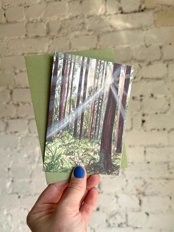 a greetings card featuring an illustration of sunlight beams coming through a woods with a green envelope
