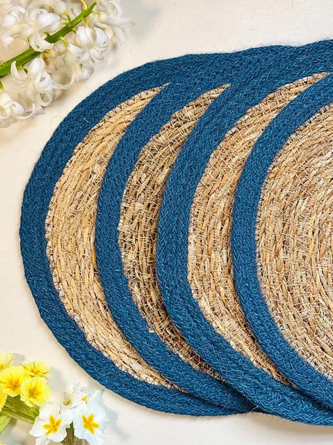 Close up of a round woven seagrass Placemats with teal rings, shown on a light surface.