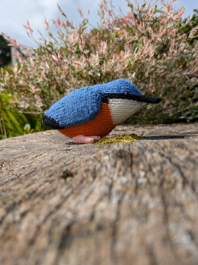 knitted nuthatch sitting on a tree stump