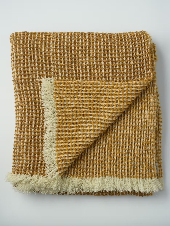 Grainne Honeycomb Lambswool Blanket. a yellow textured blanket photographed folded against a plain background.