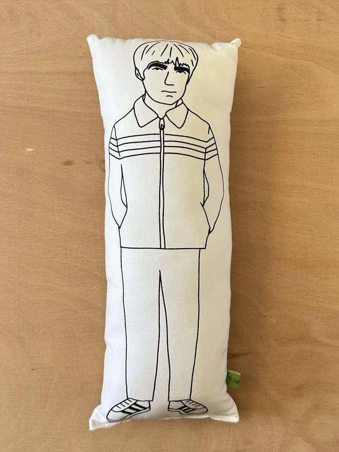 Black and white illustrated screen printed cushion of Oasis band member Noel Gallagher. The cushion is on a light wooden surface.