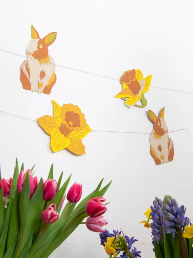 Rabbit and chick garland hung on white wall with Spring flowers in foreground