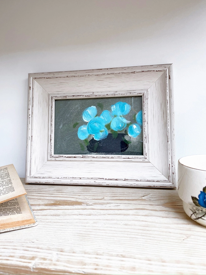 shelf display featuring framed painting of 9 blue flowers