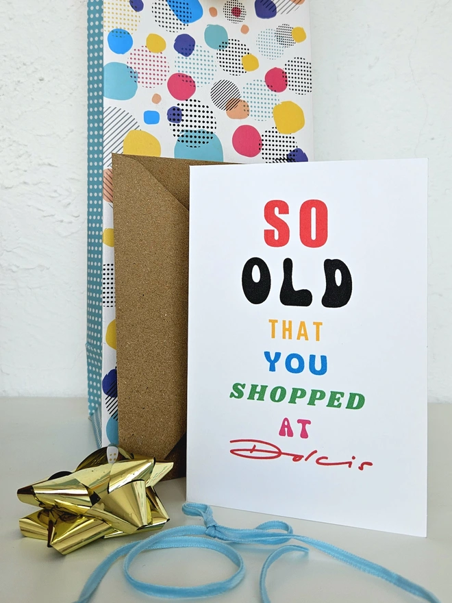 A photograph of the front of a humorous A6 greeting card illustrated using brightly coloured text and the retro shop logo. The text says so old you shopped at Dolcis
