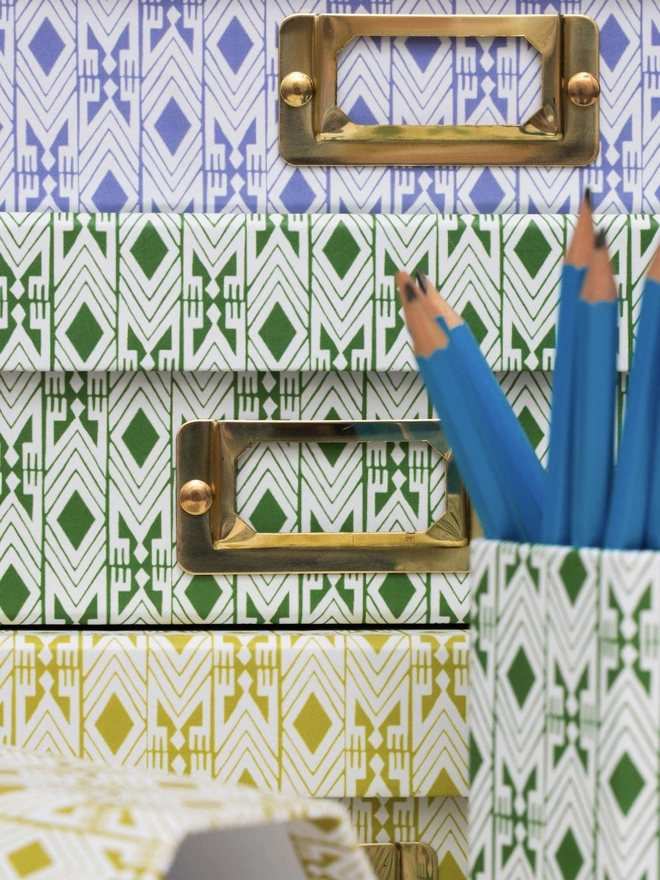 Tijan Lidded Portfolio Box, a collection of colourful portfolio boxes stacked on a plain surface. They are accompanied by a pencil pot. 