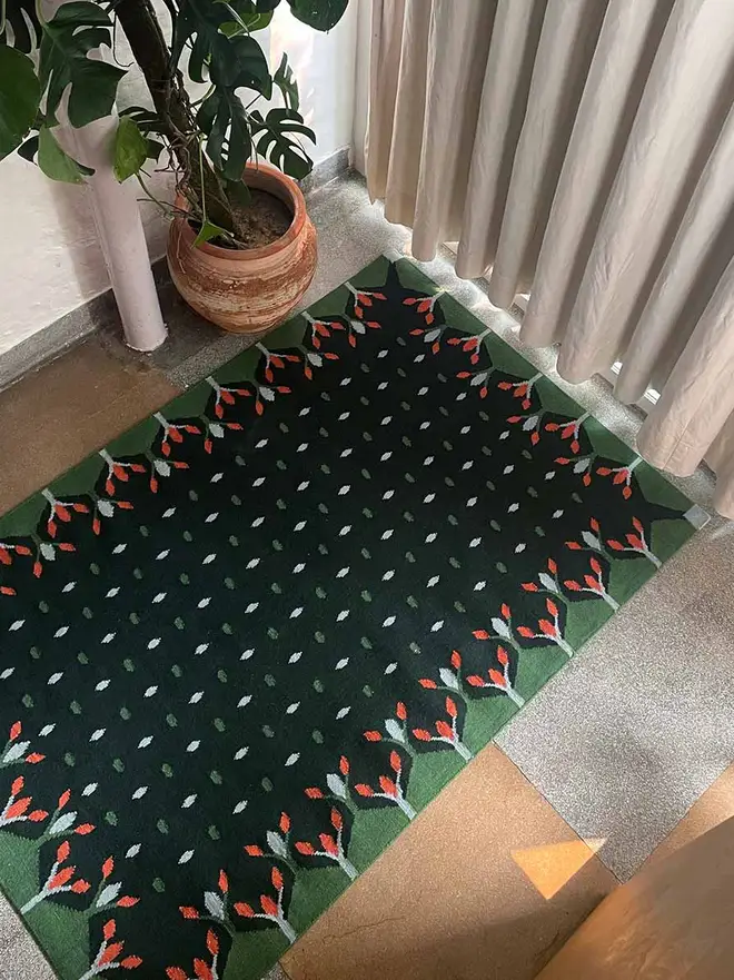 Hedgerow Flatweave Rug, a colourful rug sitting in a decorated room. It is accompanied by some household items.