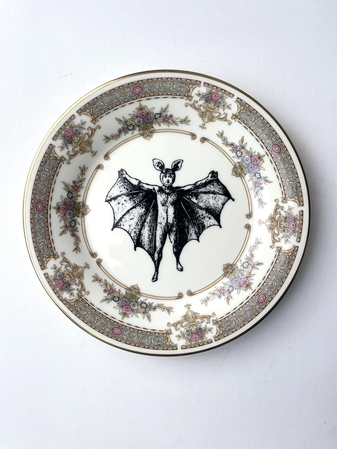 vintage plate with an ornate border, with a printed vintage illustration of a bat boy in the middle 