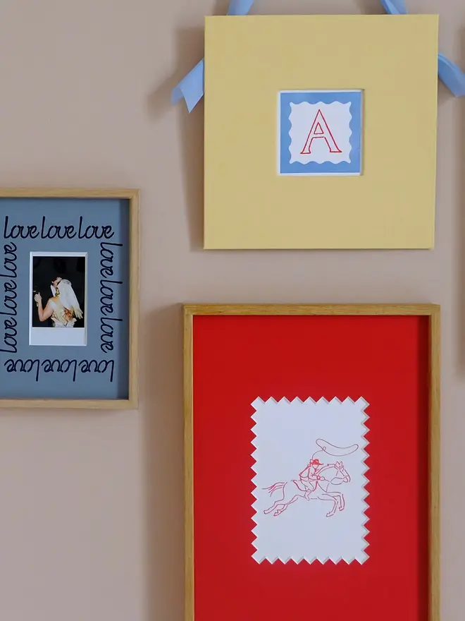 'Love' instax mini mount frame with a blue mount featuring a decorative frill border around a centered Instax Square photo, displayed on a neutral beige wall.