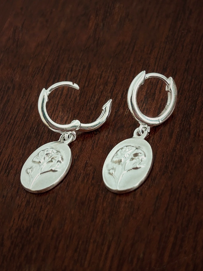 Sterling Silver Huggie drop earring with forget me not charms charms on a dark background showing the opening clasp