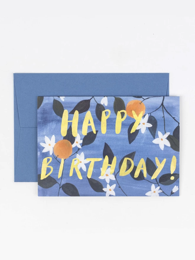 A birthday card featuring illustrated oranges and orange blossom. There is a hand lettered overlaid text that reads "Happy Birthday"