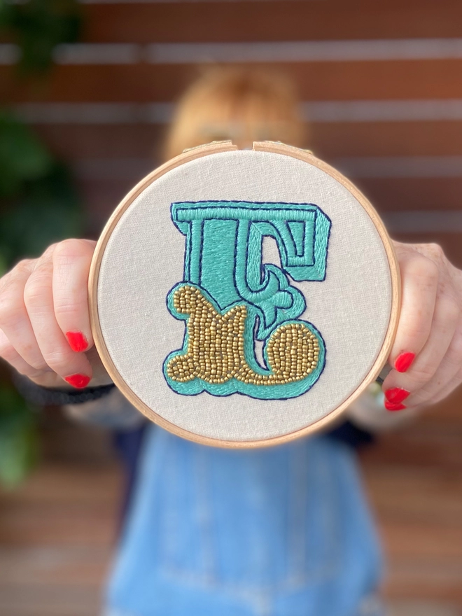 An embroidered letter E being held in front of a female