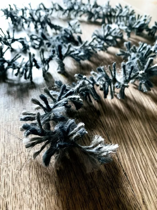End of a length of silver dyed string tinsel AKA Strinsel on an oak table, shot close up