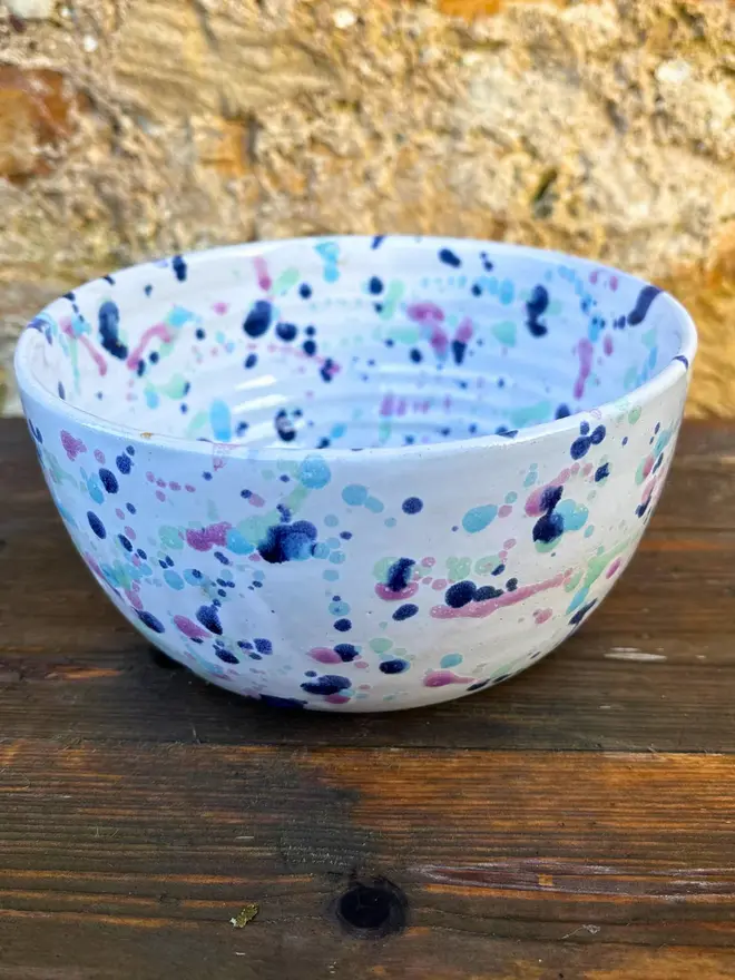 Sweetpea Small Bowl, a colourful bowl placed on a wooden surface against a brick wall. 