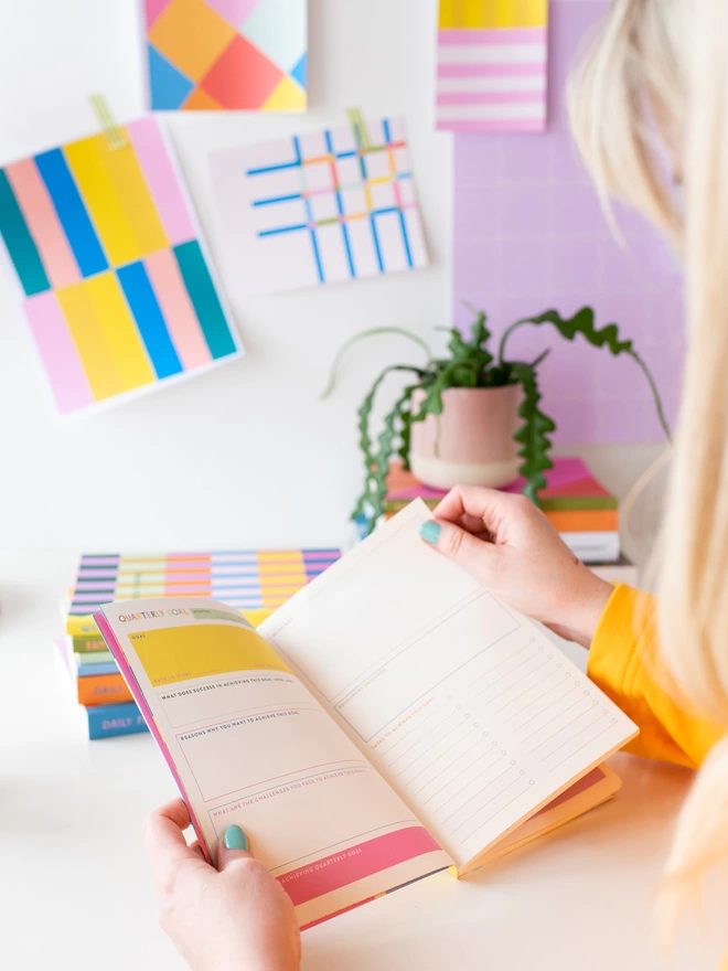 woman holds weekly planner open on colourful quarterly goal double page spread
