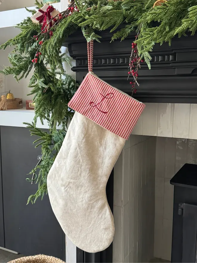 Striped Embroidered Christmas Stocking. A red and beige striped cuffed stocking hung on a mantle