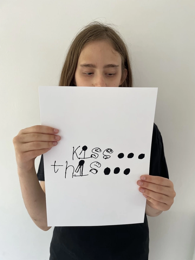 Piper holding her digital print with her unique handwritten font where she mixes lower and upper case letters and fills in her full stops to be big black dots on a white background