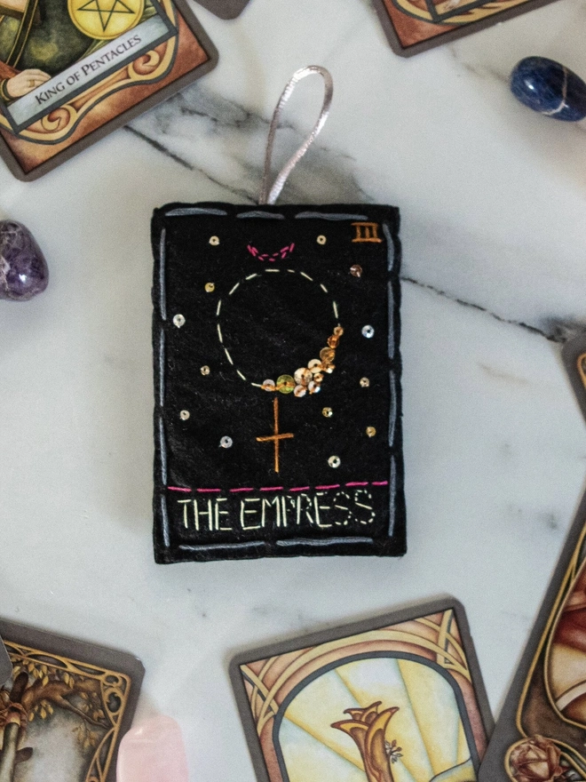 A handcrafted felt ornament with sequins and embroidery depicting "The Empress" tarot card. 