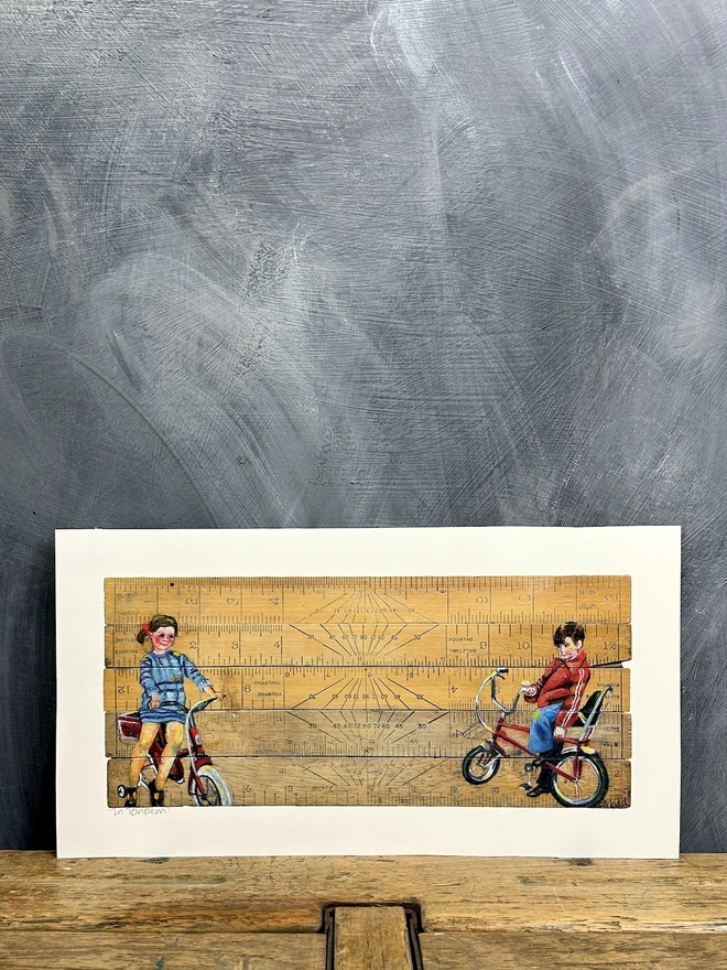 two children sitting on their bikes painted onto vintage school rulers