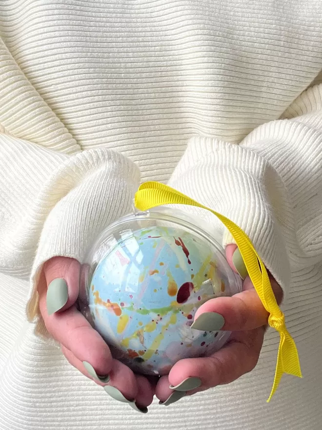 a hand holding a blue christmas ornament made out of chocolate with a yellow ribbon