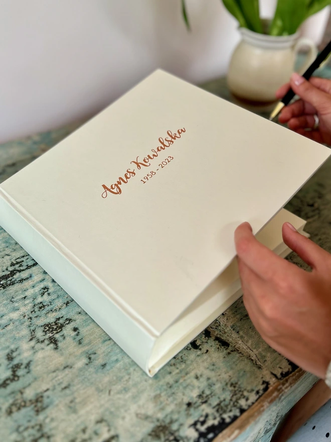 A condolence book with a name printed on the front is lying ready to be written in on a green table
