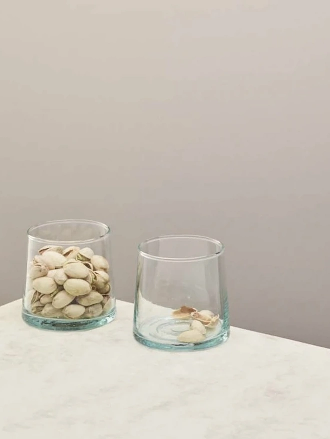 Low Glasses (Set Of 1 Or 4), a low glass sitting on a white counter top against a plain backdrop. It is filled by some nuts. 
