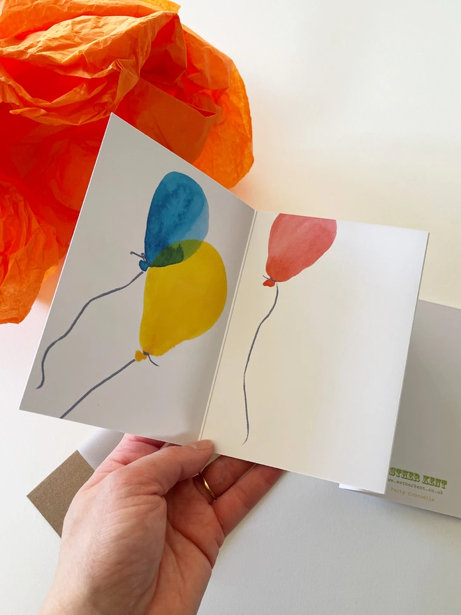Esther Kent illustrated concertina greeting card showing a creen crocodile on a white background, with colourful balloons