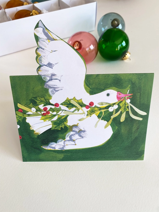 Esther Kent illustrated Christmas Card showing white goose on green inky background, carrying holly and mistletoe