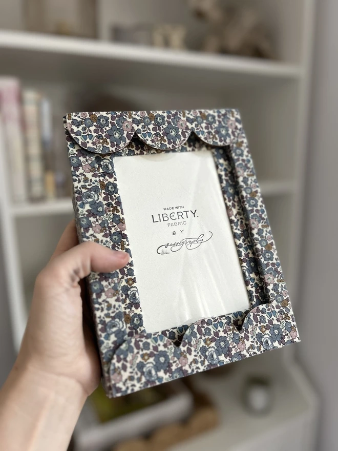 Liberty fabric covered mount frame with scallop edge held in hand against shelves