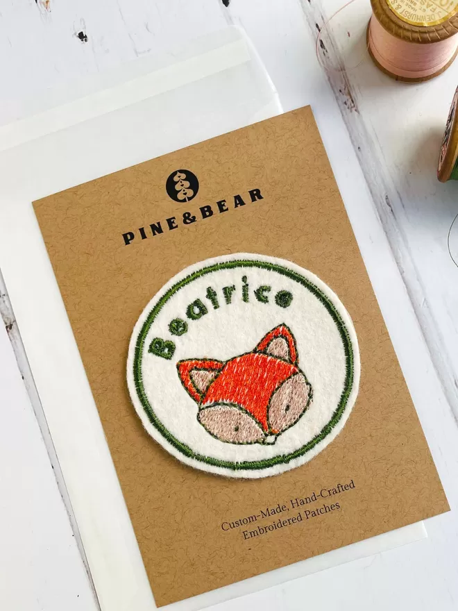 Embroidered name patch with a fox design on a presentation card.