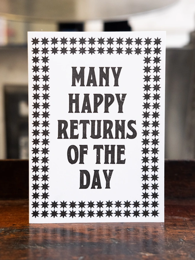 Letterpress card with text design "Many happy returns of the day," bordered by two layered pattern of 8 sided stars