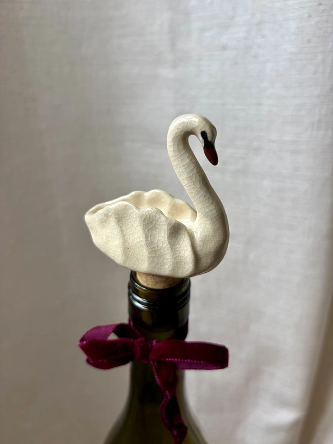 A white crackle ceramic, swan shaped bottle stopper, in a bottle of wine