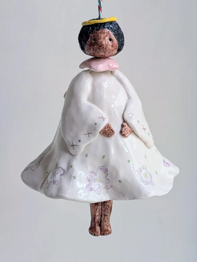 a hanging angel bell decoration with brown skin and violet floral dress in handmade white ceramic