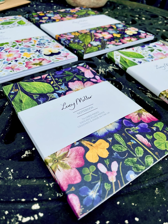 Four Nature-Inspired Floral Notebooks in lLight and Dark Flower Designs, Various Sizes, 'Lucy Miller' Branded Belly Bands, on Garden Table
