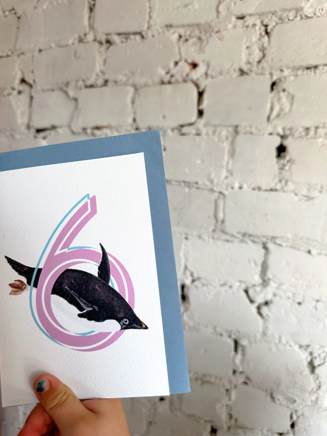 a white card with a big pink number 6 and an illustrated penguin with a blue envelope