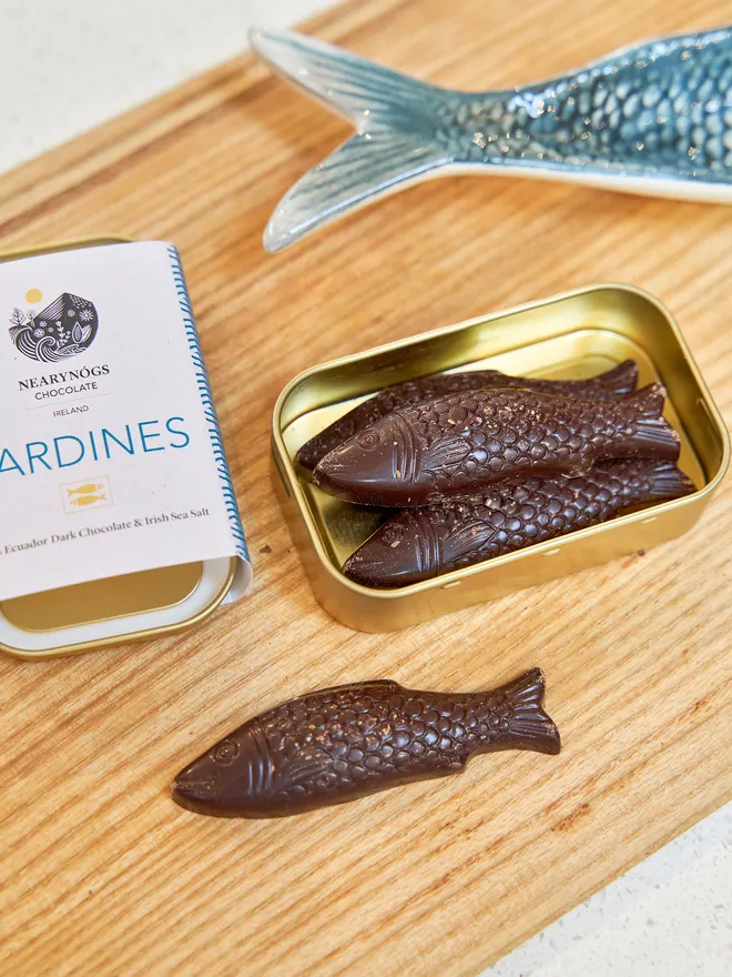 Sardines Dark Chocolate 60% (Tin Of 4), a tin of chocolate fish sitting on a wooden surface. 