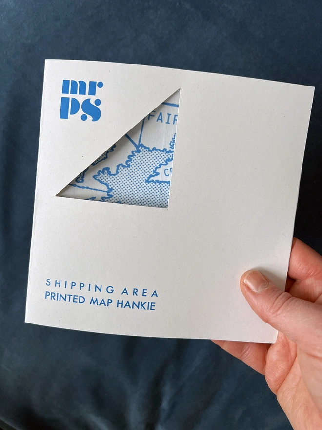 A hand holding a Mr.PS Shipping Area Map Handkerchief in its wallet packaging