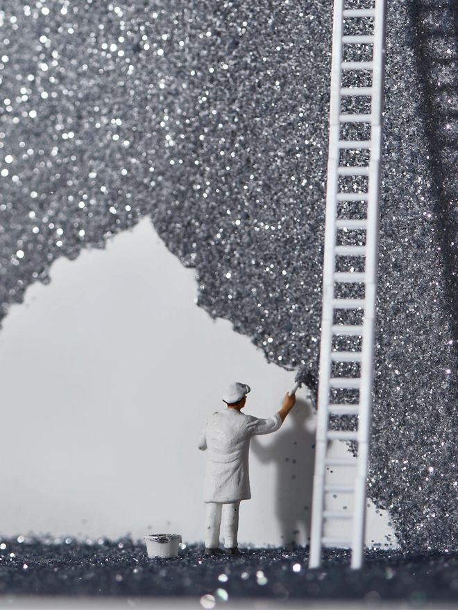 Miniature scene in an artbox showing a tiny painter figurine painting the night sky sparkling black and silver 