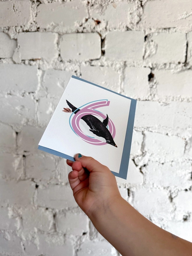 a white card with a big pink number 6 and an illustrated penguin with a blue envelope