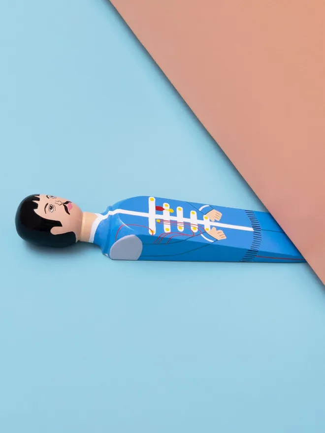 Wooden Door Stopper (Pauly), a colourful wooden door stop sitting under a door.