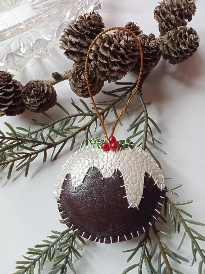 Hand stitched leatherette Christmas pudding decoration placed on a branch of small pine cones