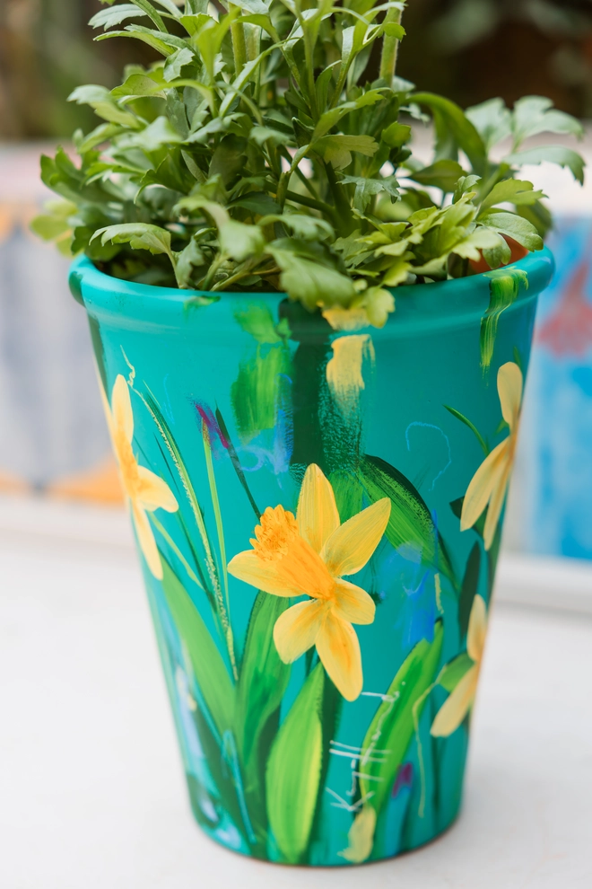 A beautifully hand painted interior terracotta plant pot. Background painted in a rich blue green adorned in vibrant Cornish Trelawney Gold daffodil flowers.