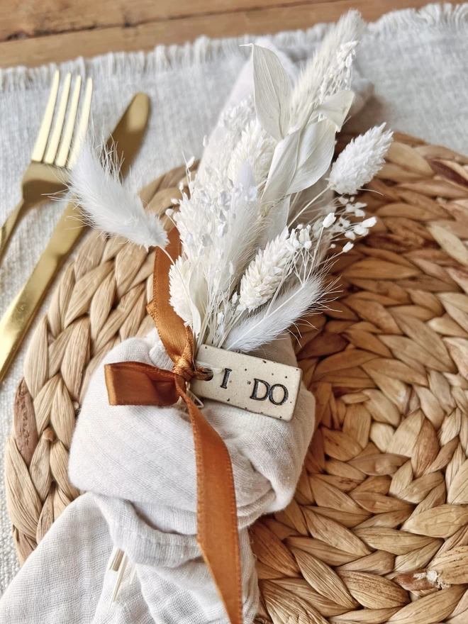 knotted napkin tied with a mini floral posy and a ceramic tag, which says 'I do'