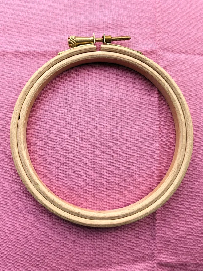 A wooden embroidery hoop lying on a piece of pink coloured fabric