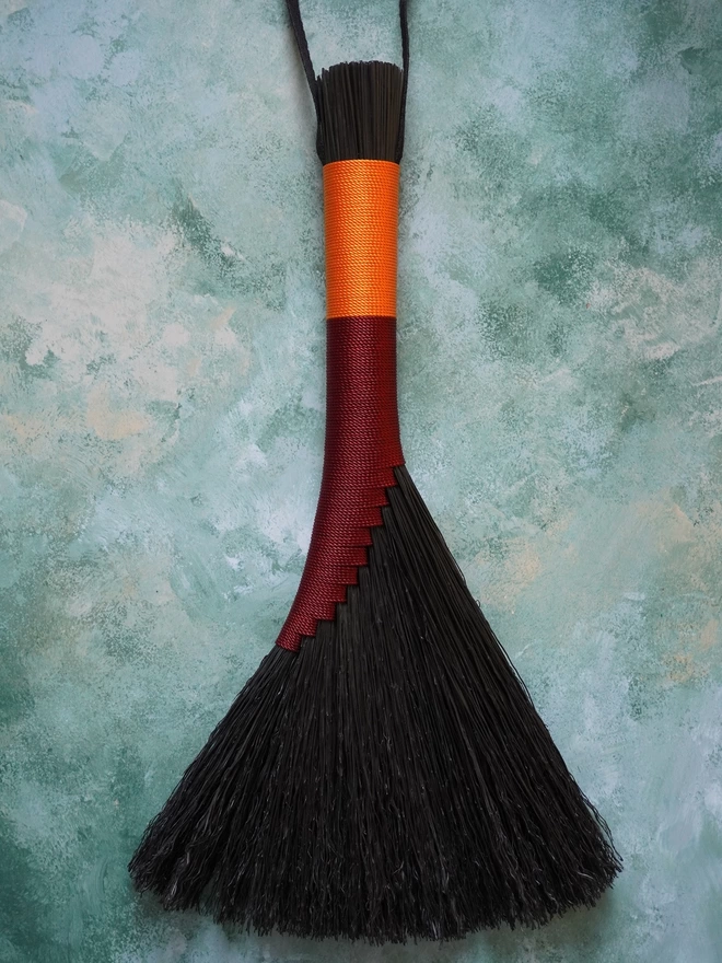 Black broomcorn handbroom with burgundy and orange nylon cord binding